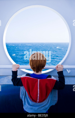 Jeune garçon de regarder à travers un trou à port la mer et l'horizon sur un ferry Banque D'Images