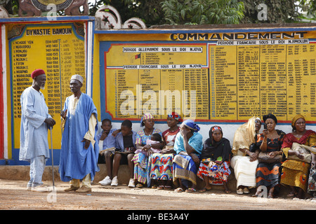 Les femmes et les hommes devant le palais du Sultan, en attente d'audience avec le Sultan, derrière eux les panneaux sur l'histoire de l'Bamu Banque D'Images