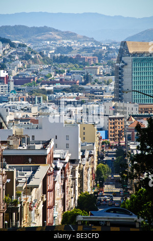 Paysage urbain de San Francisco Nob Hill Steep Street View California // SAN FRANCISCO, California — Une vue panoramique du paysage urbain de San Francisco depuis Nob Hill met en valeur son terrain vallonné emblématique et son architecture urbaine dense. L'image capture une rue escarpée descendant dans la ville, bordée d'un mélange de bâtiments résidentiels et commerciaux. Cette perspective met en valeur le paysage urbain unique de San Francisco, connu pour ses élévations spectaculaires et son développement compact. Des montagnes lointaines sont visibles sous un ciel dégagé, caractéristique de la topographie diversifiée de la région. Banque D'Images