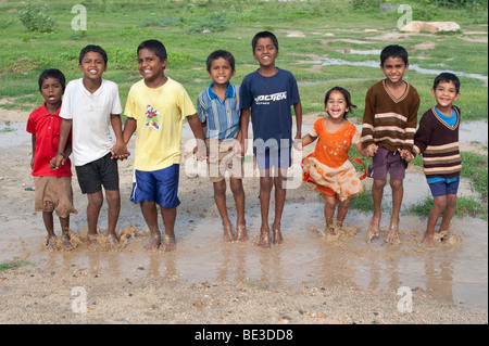 Les enfants indiens de sauter et de s'éclabousser dans une flaque d'eau dans la campagne indienne. L'Andhra Pradesh, Inde Banque D'Images