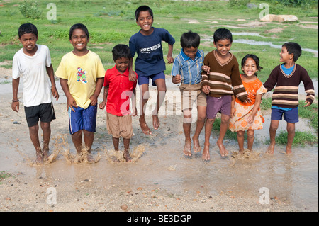 Les enfants indiens de sauter et de s'éclabousser dans une flaque d'eau dans la campagne indienne. L'Andhra Pradesh, Inde Banque D'Images