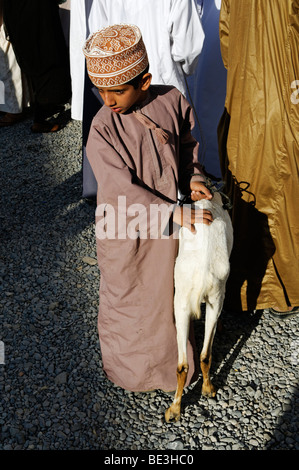 Garçon omanais en costume traditionnel au chèvre, de l'élevage des animaux ou marché à Nizwa, Hajar al Gharbi, Montagnes, région Dakhliyah Al Banque D'Images