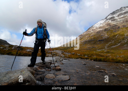 Randonneur avec sac à dos et bâtons de marche traversant une rivière dans la montagnes écossais, les Highlands écossais, Stuca Dhuibh Choeur 'Beig Banque D'Images