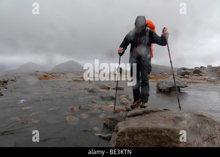 Hikerswith et pôles de randonnée et plus fluide traversant une rivière à la pluie, écossais Scottish Highlands, Ecosse, Torridon, Liathach Banque D'Images