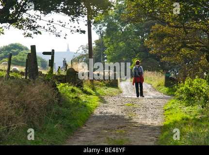 Femme walker sur ancienne route près de Hebden Bridge, avec Stoodley Pike dans la distance, Calderdale, West Yorkshire, England UK Banque D'Images