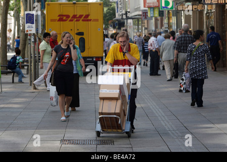 Transporteur de colis Michael Meindel l'équilibre entre une pile de paquets dans la rue avec son chariot pour l'allemand Deutsche Post mail Banque D'Images