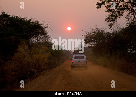 Véhicule à quatre roues motrices roulant sur une piste sans fin vers le coucher du soleil, la Zambie, l'Afrique Banque D'Images
