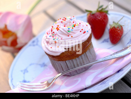 Muffin Cupcake à la crème, des fraises et sucre perlé sur la plaque Banque D'Images