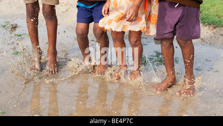 Les enfants indiens de sauter et de s'éclabousser dans une flaque d'eau dans la campagne indienne. L'Andhra Pradesh, Inde Banque D'Images