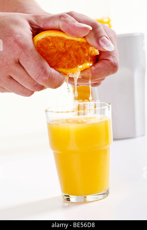 Serrant la main d'une demi-orange dans un verre de jus d'orange Banque D'Images