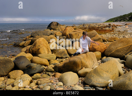 Tourist Traveler pointant sur des blocs de couleur rouille sur la rive du golfe de Martins Point le Saint-laurent Océan Atlantique Terre-Neuve Canada Banque D'Images