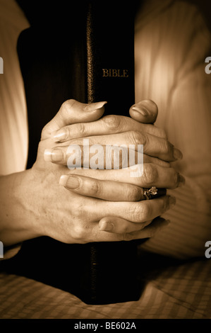 Bible et la femme les mains jointes ensemble dans la prière dans un style vintage Banque D'Images