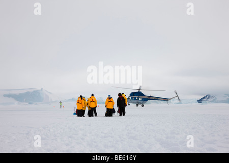 Les photographes de voyage antarctique recueillir sur la glace le bouchon avant de vol en hélicoptère vêtus de vestes parka jaune vif Banque D'Images