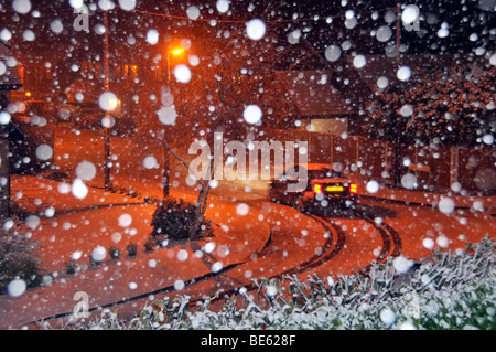 Flocons de neige par flash avec éclairage éclairage orange couverts de neige paysage de rue résidentielle pour les conducteurs de voitures le long de la route Banque D'Images