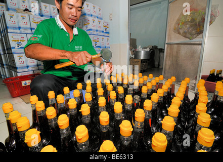 L'homme vietnamiens mettre des bouchons en plastique jaune sur les bouteilles en verre de la sauce de poisson traditionnel vietnamien, Nuoc Mam Phu Quoc, Vietna Banque D'Images