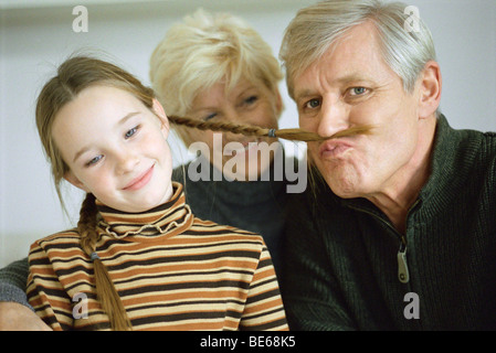 Jeune fille avec des grands-parents, grand-père à l'aide de la natte de fille d'imiter la moustache Banque D'Images