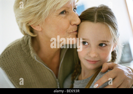 Hauts femme avec bras autour de sa petite-fille, embrassant le front, portrait Banque D'Images