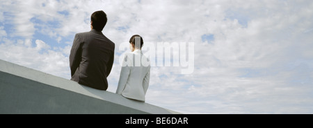 Businessman and businesswoman assis côte à côte sur le rebord du toit Banque D'Images