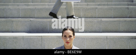 Businesswoman sur mesures, looking at camera, homme qui marche en arrière-plan Banque D'Images