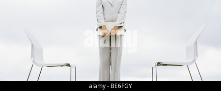 Femme debout entre deux chaises holding laptop computer, cropped Banque D'Images