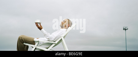 Man relaxing in transat, holding up Coffee cup Banque D'Images