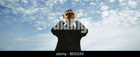 Businessman using binoculars, cloudscape en arrière-plan Banque D'Images