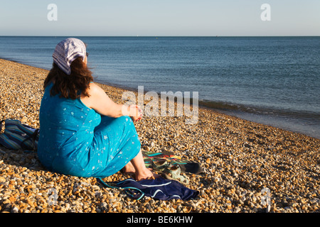 Une femme assise à contempler la mer tranquille sur la plage de Seaford, Sussex, England, UK. Banque D'Images