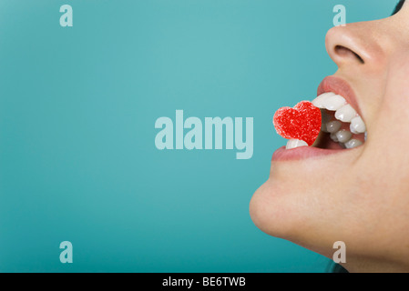 Femme tenant des bonbons en forme de coeur entre les dents, cropped Banque D'Images