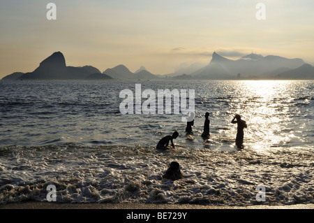 Les jeunes dans l'océan et vue sur le Pain de Sucre et Corcovado, Niteroi, Rio de Janeiro, Brésil, l'Ame Banque D'Images