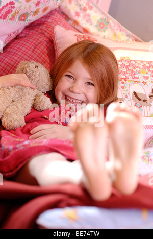 Petite fille couchée sur un canapé coussin et riant, barefoot Banque D'Images