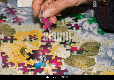 Trouver le bon endroit. Une personne âgée cherche une place pour une seule pièce d'un puzzle. Pièces du puzzle sont dispersés Banque D'Images