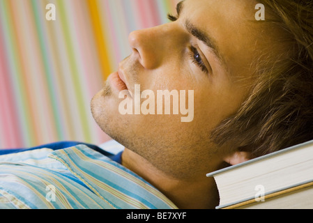 Jeune homme rêverie, resting head on pile de livres Banque D'Images