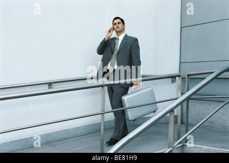 Businessman walking on sidewalk using cell phone, carrying briefcase Banque D'Images