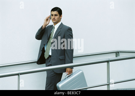 Businessman walking on sidewalk using cell phone, carrying briefcase Banque D'Images