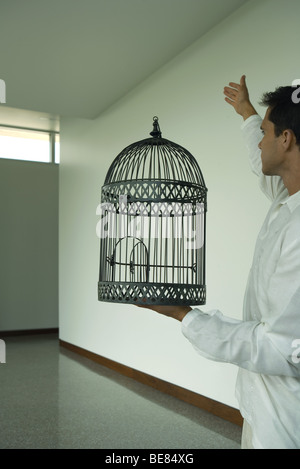 Man holding empty cage à oiseaux avec porte ouverte, bras levé, side view Banque D'Images