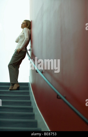 Femme debout du haut des escaliers, leaning against wall, looking away Banque D'Images