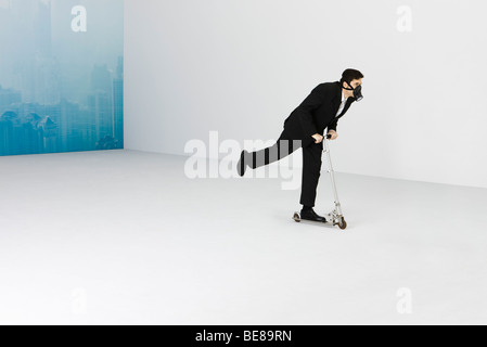 Businessman wearing gas mask équitation pousser scooter, cityscape obscurci par le smog en arrière-plan Banque D'Images