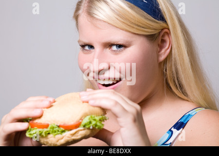 Jeune femme obèse est en train de manger un hamburger de restauration rapide. Banque D'Images