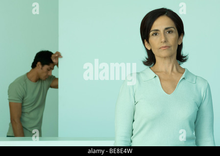 Woman looking at camera avec l'air de déception, l'homme avec tête baissée leaning against wall en arrière-plan Banque D'Images