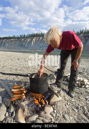 La cuisine femme sur un feu de camp, barbecue, saucisses Bratwurst, électrique, pot, grill, Upper Liard River, Yukon Territory, Canada Banque D'Images