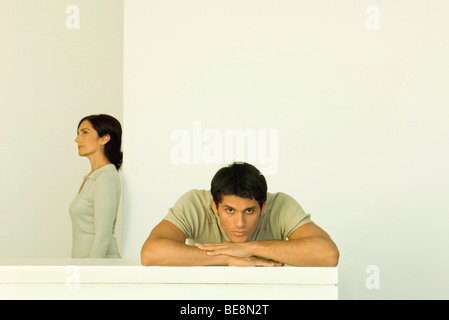 Man resting head on arms looking at camera, woman in background looking away Banque D'Images