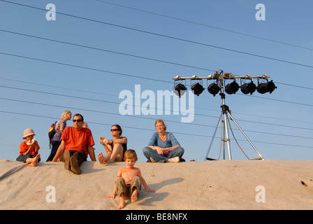 Visiteurs Fistival assis sur un talus de l'Elbwiese prairie à côté d'une rangée de projecteurs pour le grand feu de camp et la mus Banque D'Images