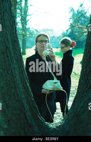 Femme debout à côté de tronc d'arbre, à l'aide de téléphone fixe Banque D'Images