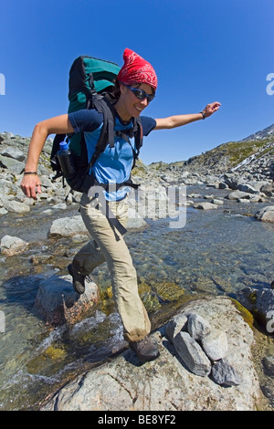 Jeune femme sautant à travers un ruisseau, randonnées, randonnée, randonneur avec sac à dos, de la Piste-chilkoot historique, le col Chilkoot, près de l'Am Banque D'Images