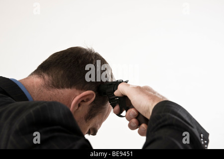 Homme portant un costume, tenant sa tête à des armes à feu Banque D'Images