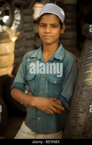 Un garçon s'appuie contre un pneu à l'extérieur d'une boutique dans le bazar de pièces de voiture (ou marché des pièces de rechange) dans la région de Old Delhi, Inde Banque D'Images