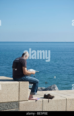 Homme assis sur le mur avec des chaussures reading newspaper sur sunny day Banque D'Images