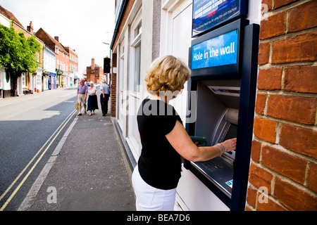 BARCLAYS BANK UN TROU DANS LE MUR DANS LA MACHINE UNE RUE PRINCIPALE . Une FEMME PREND DE L'ARGENT. Banque D'Images