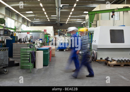 Deux ouvriers marchant à travers une usine, blurred motion, long exposure Banque D'Images