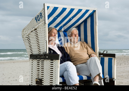 Un couple assis ensemble dans une chaise de plage à capuchon Banque D'Images